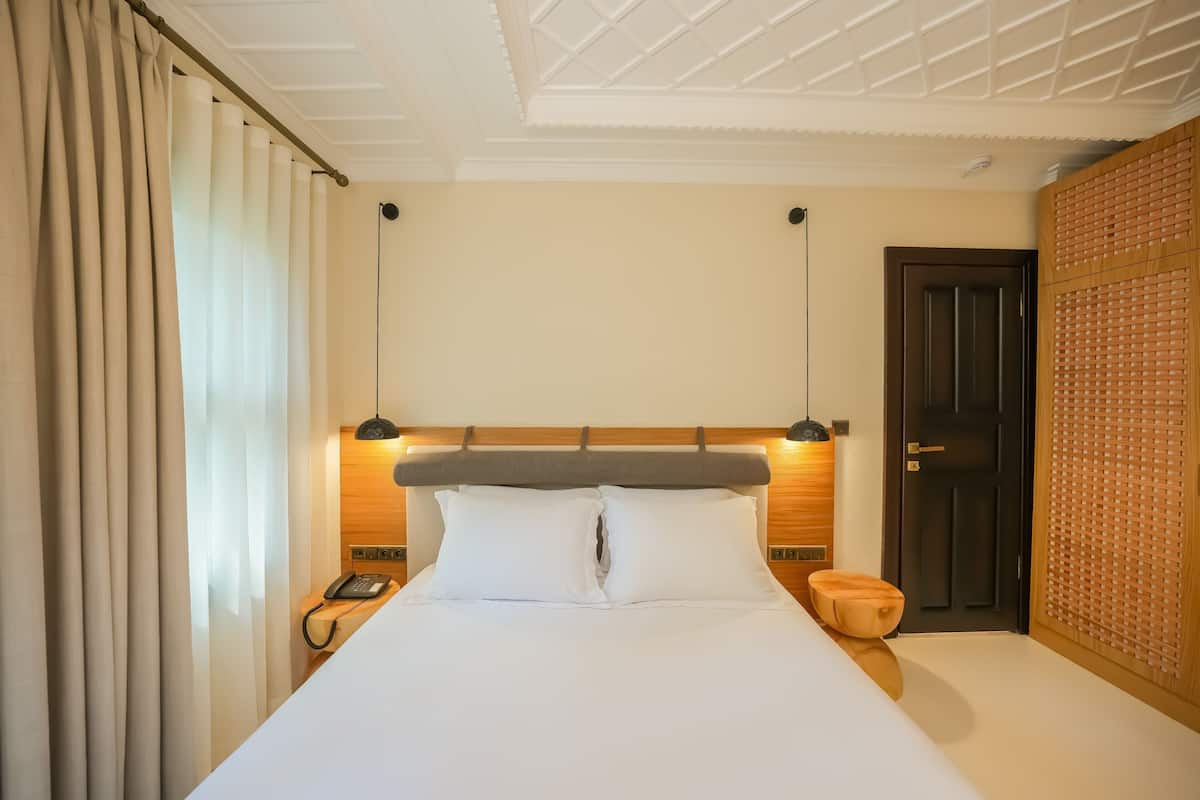 A hotel room with a bed, bedside lamp, wooden headboard, and a door with a wooden panel.