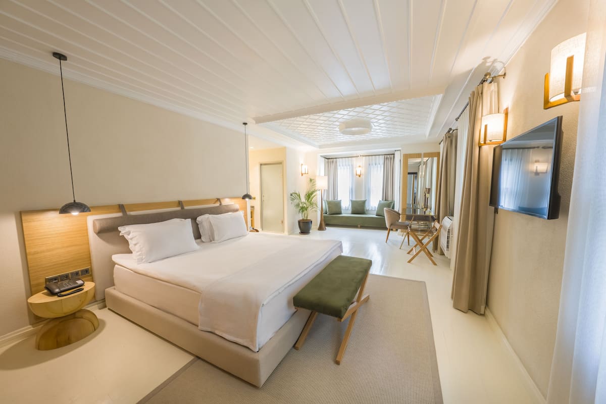 A modern hotel room with a large bed, bedside table, lamp, and a flat-screen TV mounted on the wall.