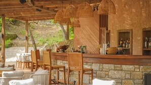 A covered outdoor seating area with wicker chairs and tables, a stone wall, and a bar with bottles. - Nuup Hotel (Marmaris)