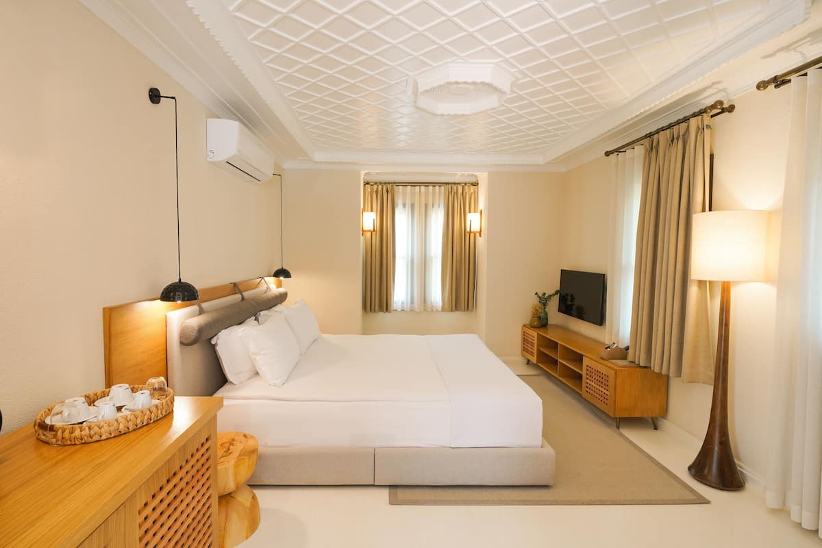A hotel room with a bed, a TV, a lamp, a wooden side table, and a ceiling with a grid pattern.