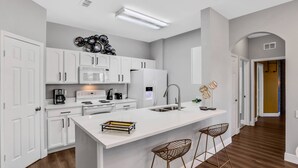 Une cuisine moderne avec des meubles blancs, un grand îlot central doté de tabourets et un four à micro-ondes.
