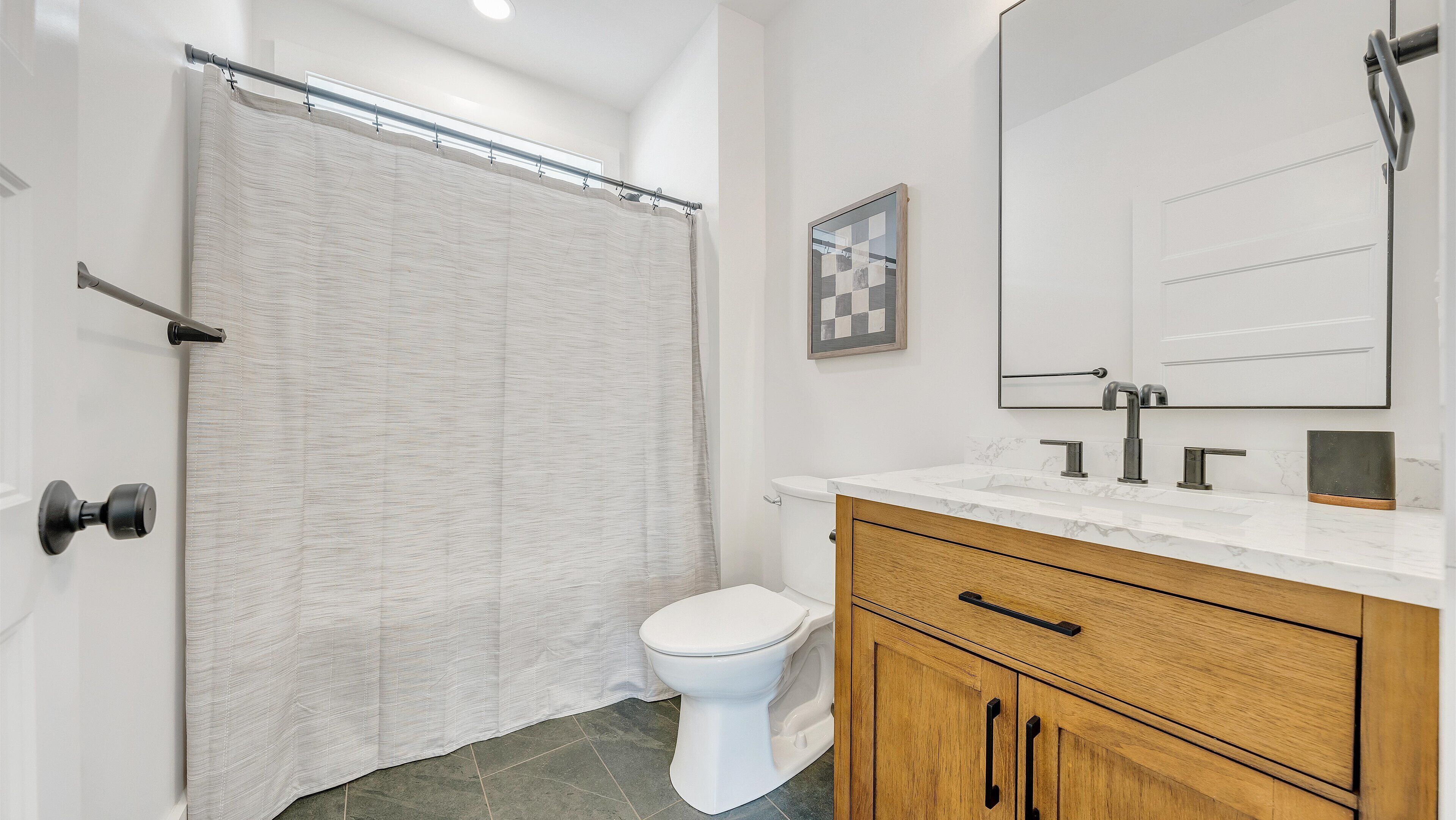Une salle de bain équipée d’une douche avec rideau, de toilettes, d’un meuble-lavabo avec miroir et d’un placard.