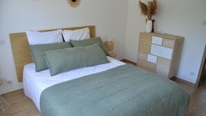 A neatly made bed with a green bedspread and pillows, a wooden headboard, a bedside table with a lamp, and a dresser with drawers. - Haut de Villa, Calme, vue mer (Serra-di-Ferro)