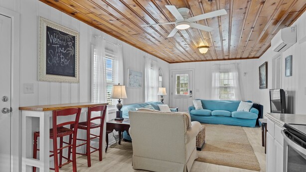 A cozy living room with a blue sofa, a wicker chair, a wooden ceiling, and a chalkboard sign. - The Saltbox-Home in Atlantic Beach (Atlantic Beach)