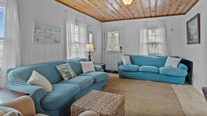 A living room with two blue sofas, a wicker ottoman, and a wooden ceiling. - The Saltbox-Home in Atlantic Beach (Atlantic Beach)