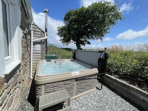 A hot tub with stone walls, a wooden ladder, and a tree in the background. - Dairy Cottage (Whitland)