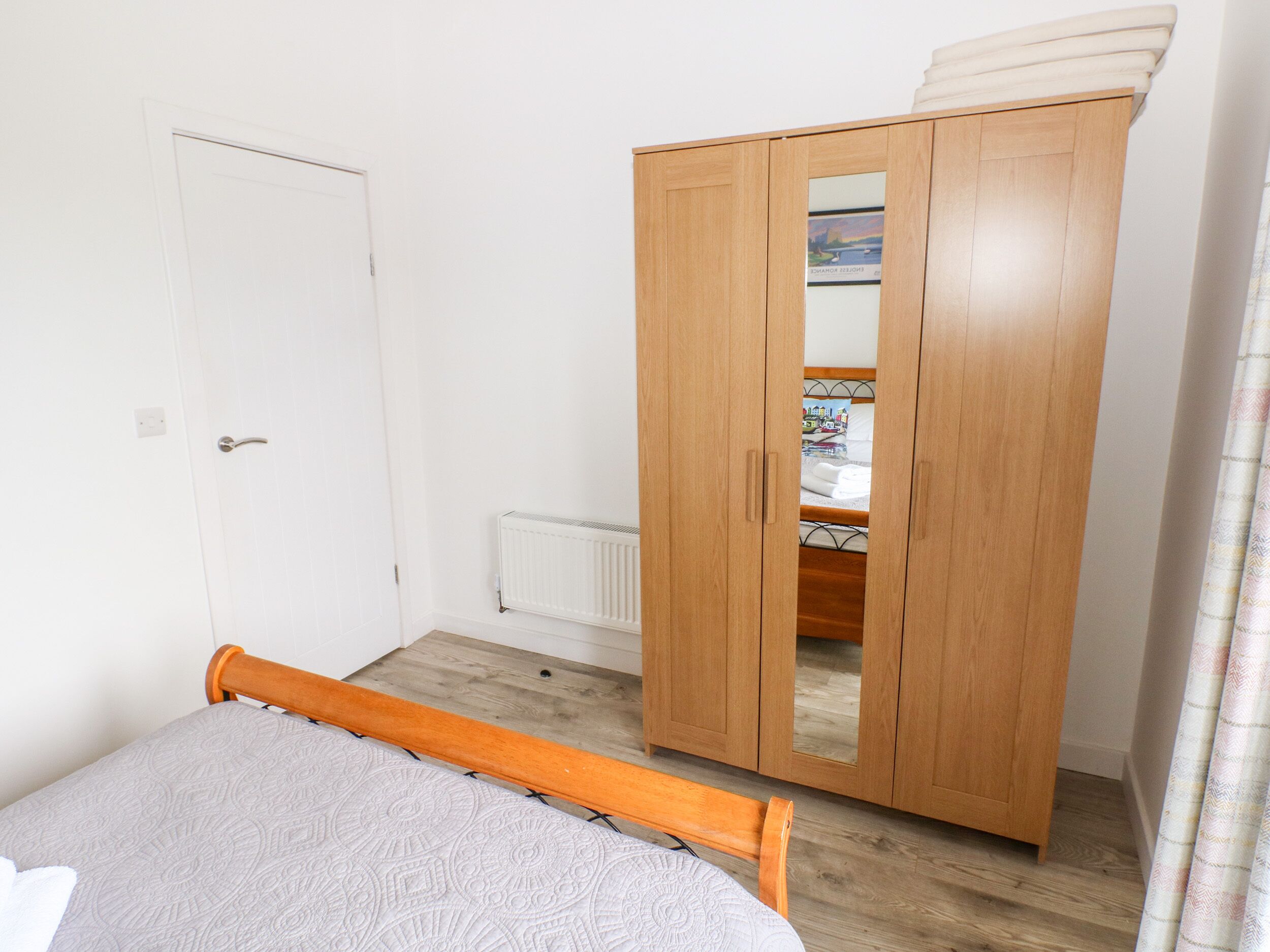 A bedroom with a wooden wardrobe, a bed with a patterned bedspread, and a radiator.
