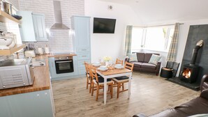 A modern kitchen with a dining area, a living room with a sofa, and a fireplace. - Dairy Cottage (Whitland)