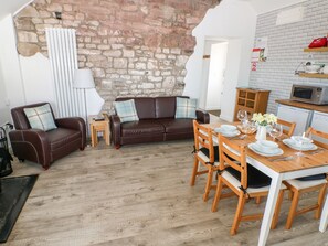A cozy living room with a brown leather sofa, a wooden dining table set for four, and a kitchen area with a microwave and a refrigerator. - Dairy Cottage (Whitland)