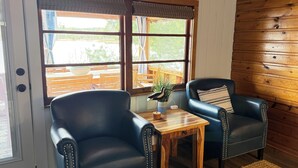 Ein Zimmer mit zwei Ledersesseln, einem Holztisch und Blick durch große Fenster.