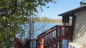 Eine Holterrasse führt zu einer Hütte am See, ein Klimagerät ist sichtbar.