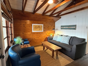 Una habitación acogedora con paredes de madera, un sofá, una mesita de centro y una silla azul.