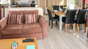 Un salon moderne comprenant un canapé, une table à manger avec des chaises, un coin cuisine équipé d’appareils électroménagers et une vue sur l’extérieur.