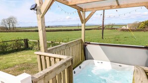 Un bain à remous installé sous une pergola en bois, offrant une vue sur un champ verdoyant et des collines lointaines.