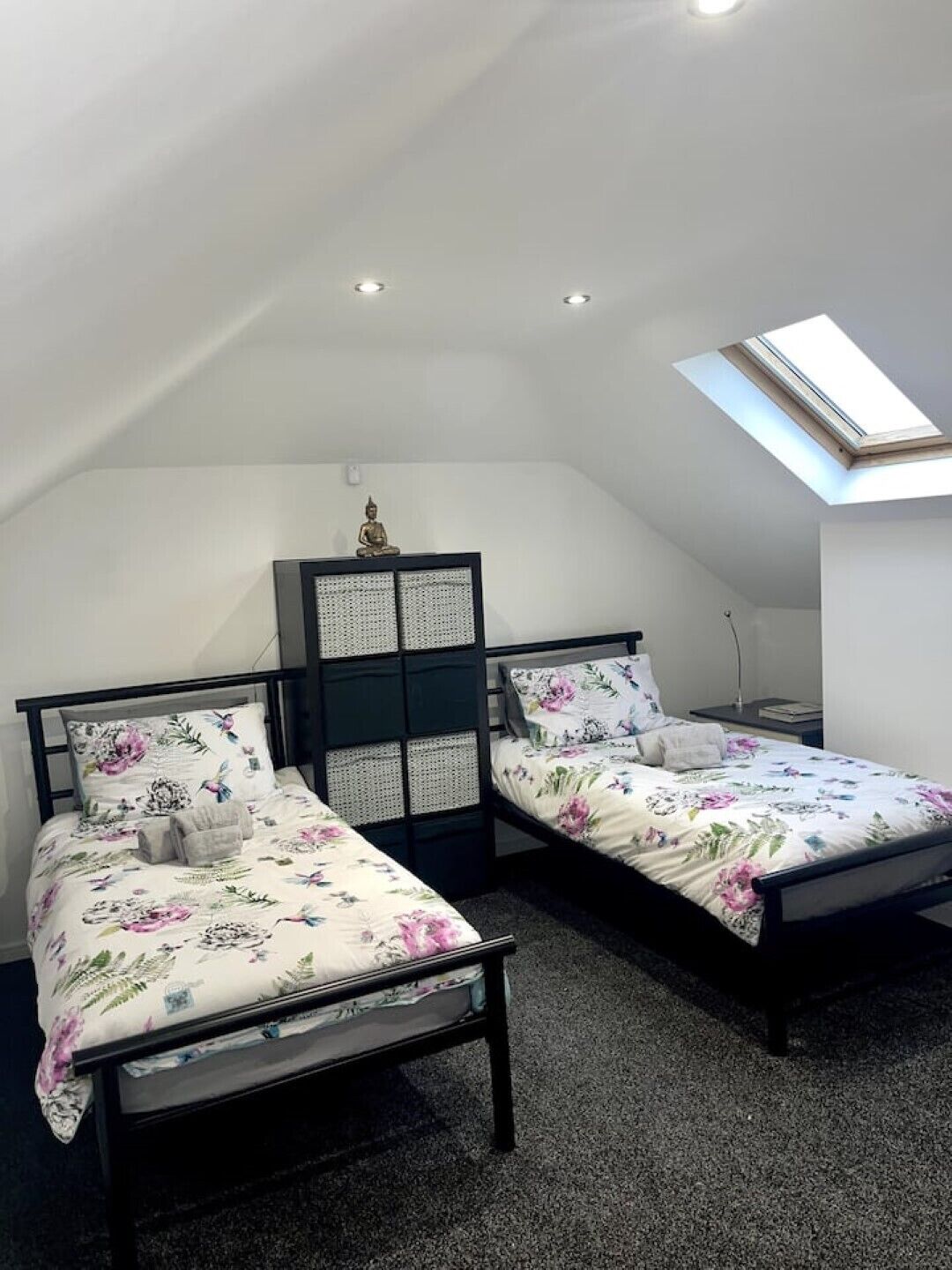 Un dormitorio con dos camas, un tragaluz y una pequeña estatua sobre un mueble.