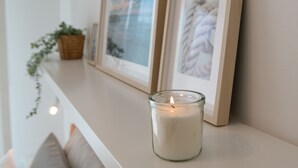 Een brandende kaars op een plank met ingelijste foto's en een plant.