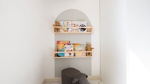 Een hoekje met een klein boekenrek, een teddybeer en een grijze kussen.