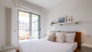 Een slaapkamer met een groot bed, een houten hoofdbord, een witte gewatteerde spreideken en uitzicht buiten door een schuifdeur van glas.