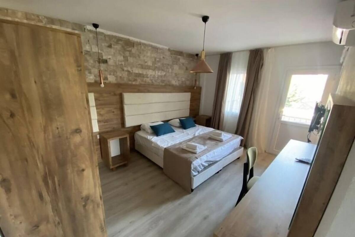 A bedroom with a wooden headboard, a bed with white linens, a nightstand, and a desk with a chair.