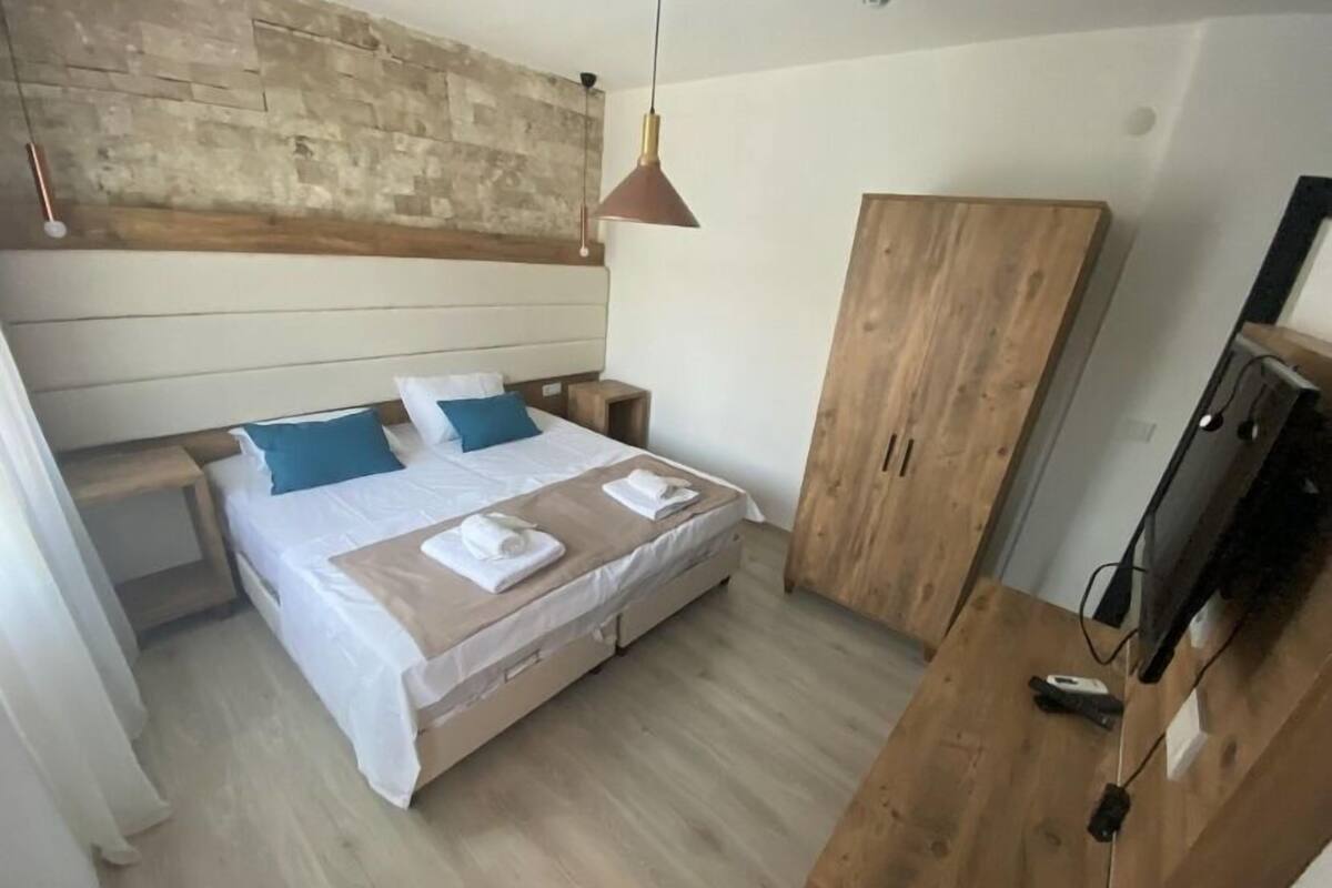 A bedroom with a bed, wooden wardrobe, and a TV.