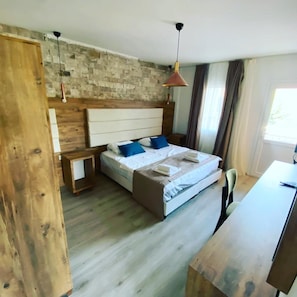 Un dormitorio con cabecera de madera, cama con ropa de cama azul y blanca, un escritorio con silla y una ventana con cortinas.