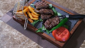 A tray with grilled meat, fries, lettuce, and a tomato on a marble surface. - Cat Kapi Alacati (Cesme)