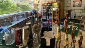 A bar area with a view of greenery, shelves with bottles, and decorative figures. - Cat Kapi Alacati (Cesme)