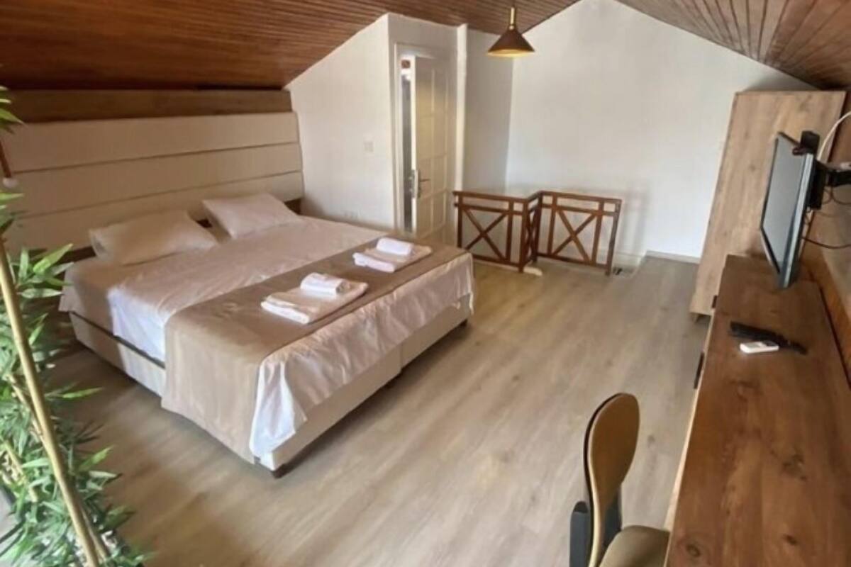 A cozy bedroom with a bed, a desk, and a chair, featuring wooden floors and a sloped ceiling.