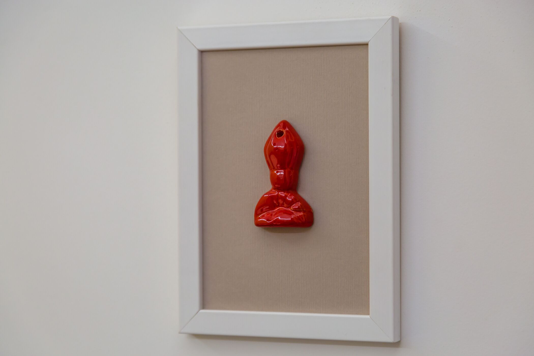 Une sculpture rouge encadrée, accrochée à un mur sobre.