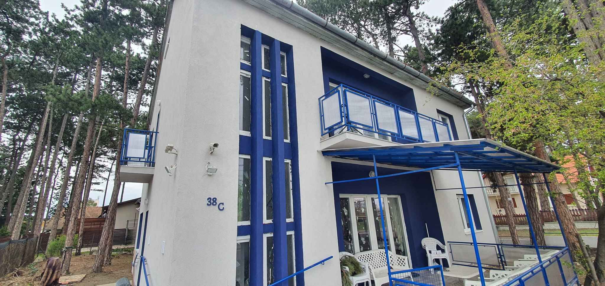 Ein zweistöckiges Gebäude mit weißer Fassade und blauen Akzenten, inklusive Balkon und Geländern.