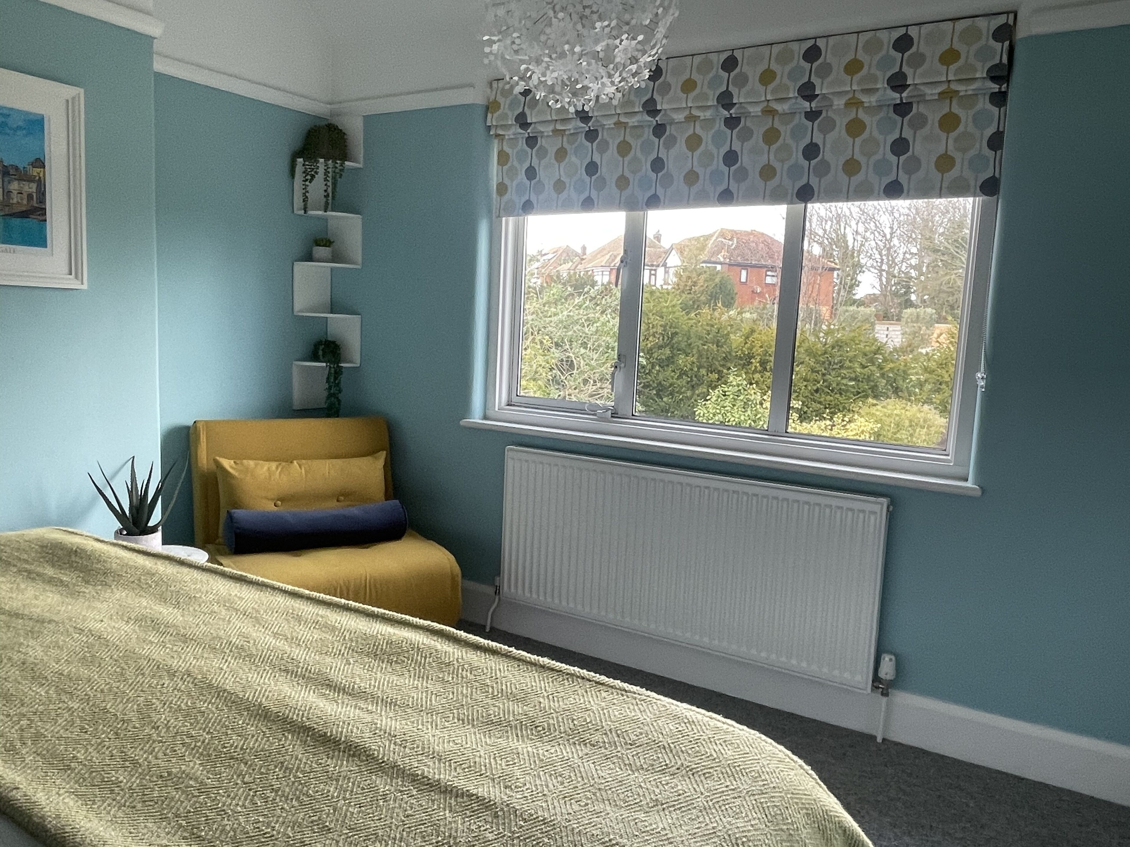 A bedroom with a bed, a window with a view, a radiator, and a plant.