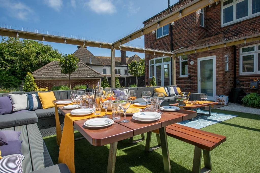 Een terras buiten met een eettafel, gedekt voor een maaltijd, omringd door een overdekte zithoek en een bakstenen gebouw op de achtergrond.