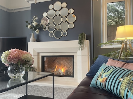 A modern living room with a fireplace, a wall-mounted mirror art piece, and a sofa with decorative pillows.