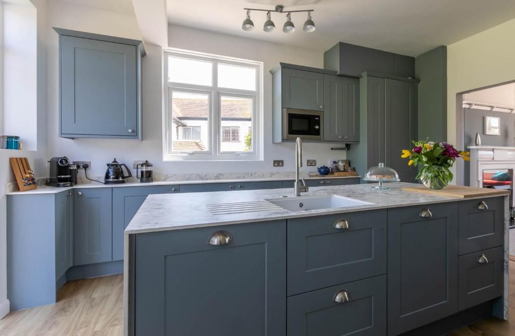 A modern kitchen with grey cabinets, a central island with a sink, and a window providing natural light.