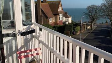 A balcony with a red chair and a white railing overlooking a residential street and the sea.