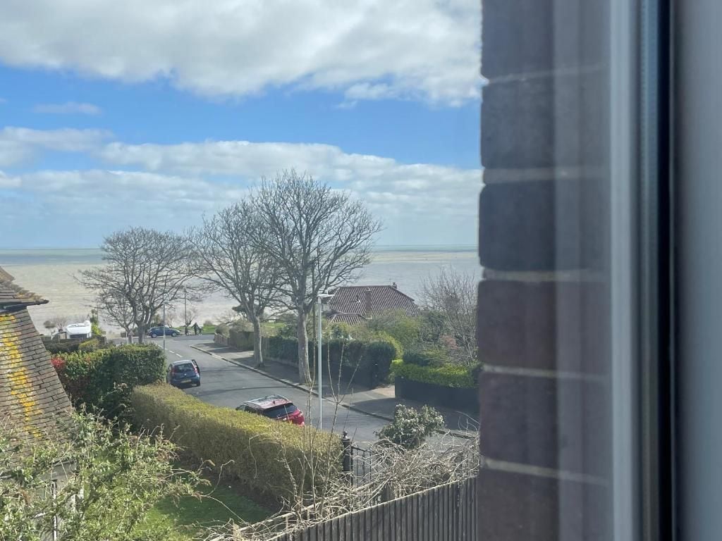 Una strada residenziale con case, un'auto parcheggiata e vista sul mare.