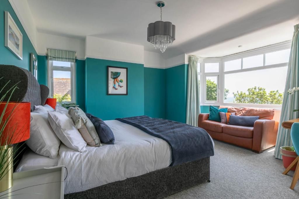 A bedroom with a bed, a sofa, a window, and a chandelier.