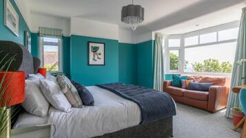 A bedroom with a bed, a sofa, a window, and a chandelier.