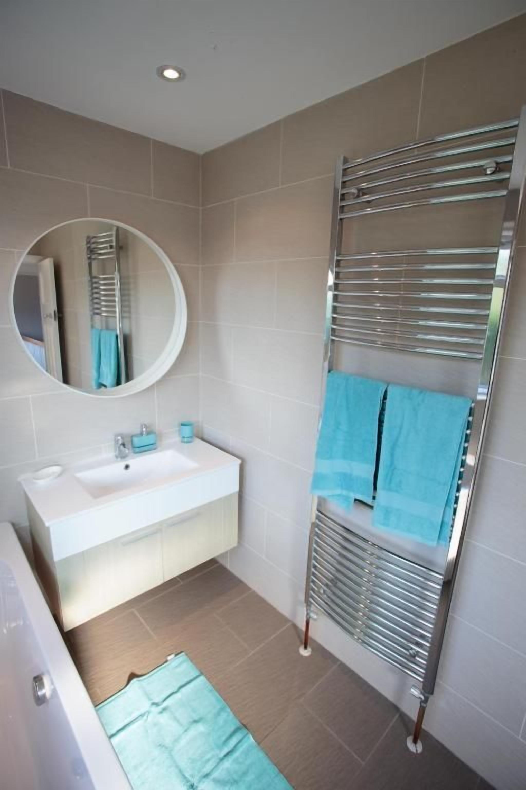 A bathroom with a white sink, a round mirror, a towel rack with two towels, and a shower area.
