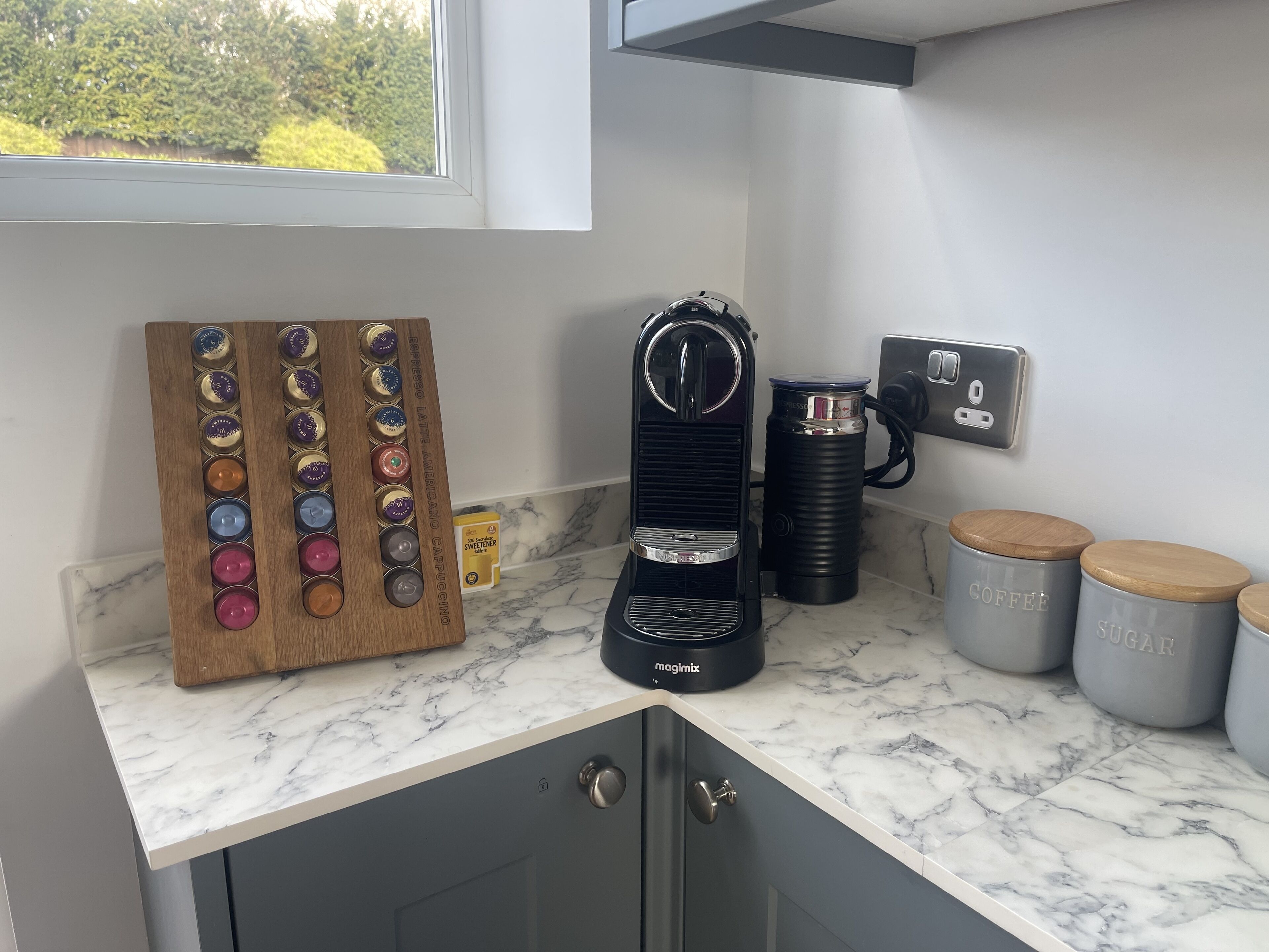 Une cuisine équipée d’une machine à café, d’un moulin à café et d’une planche en bois contenant des dosettes de café.