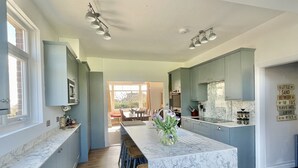 A modern kitchen with marble countertops, a central island with stools, and a view to the dining area. - Winterstoke View, Family and dog Friendly Beach Retreat (Ramsgate)