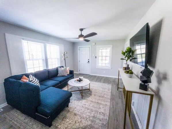 A living room with a sectional sofa, a round coffee table, a TV on a stand, and a ceiling fan.
