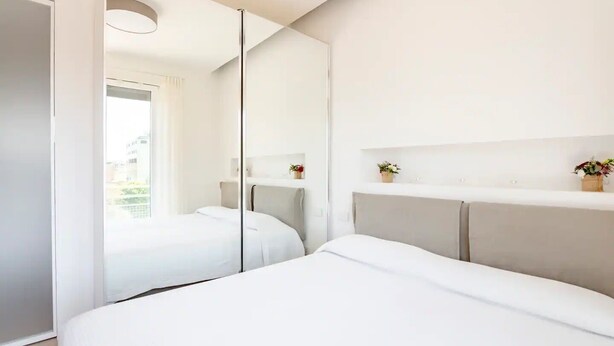 Ein modernes Hotelzimmer mit einem großen Bett, einem Nachttisch, einem Spiegel und Blick ins Freie.