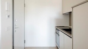 Eine schmale Küche mit weißer Tür, einem eingebauten Backofen und einer Edelstahl-Dunstabzugshaube.