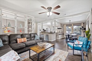 Una sala de estar moderna con un sofá, una mesa de centro y un sillón azul. Se ve una cocina al fondo con un comedor.