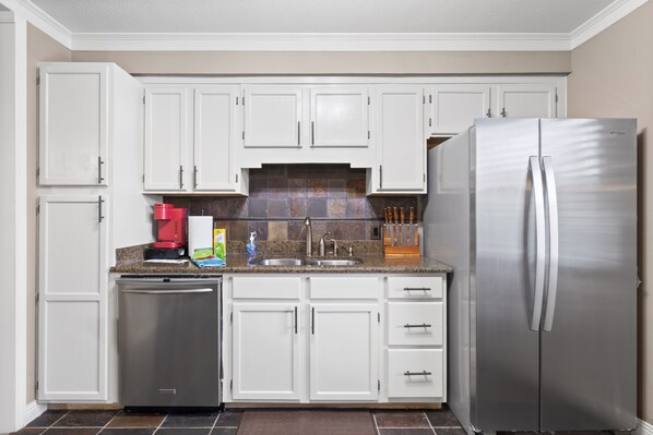 Cocina con armarios blancos, un refrigerador de acero inoxidable y un lavavajillas.