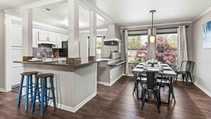 Een moderne keuken met een centraal eiland, barkrukken en een eethoek met een tafel voor vier personen.