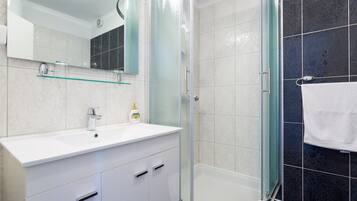 Un bagno moderno con cabina doccia in vetro, un lavandino bianco con specchio sopra e un porta asciugamani con un asciugamano bianco.