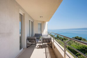Uma varanda com vista para o mar, uma mesa com cadeiras e um corrimão.