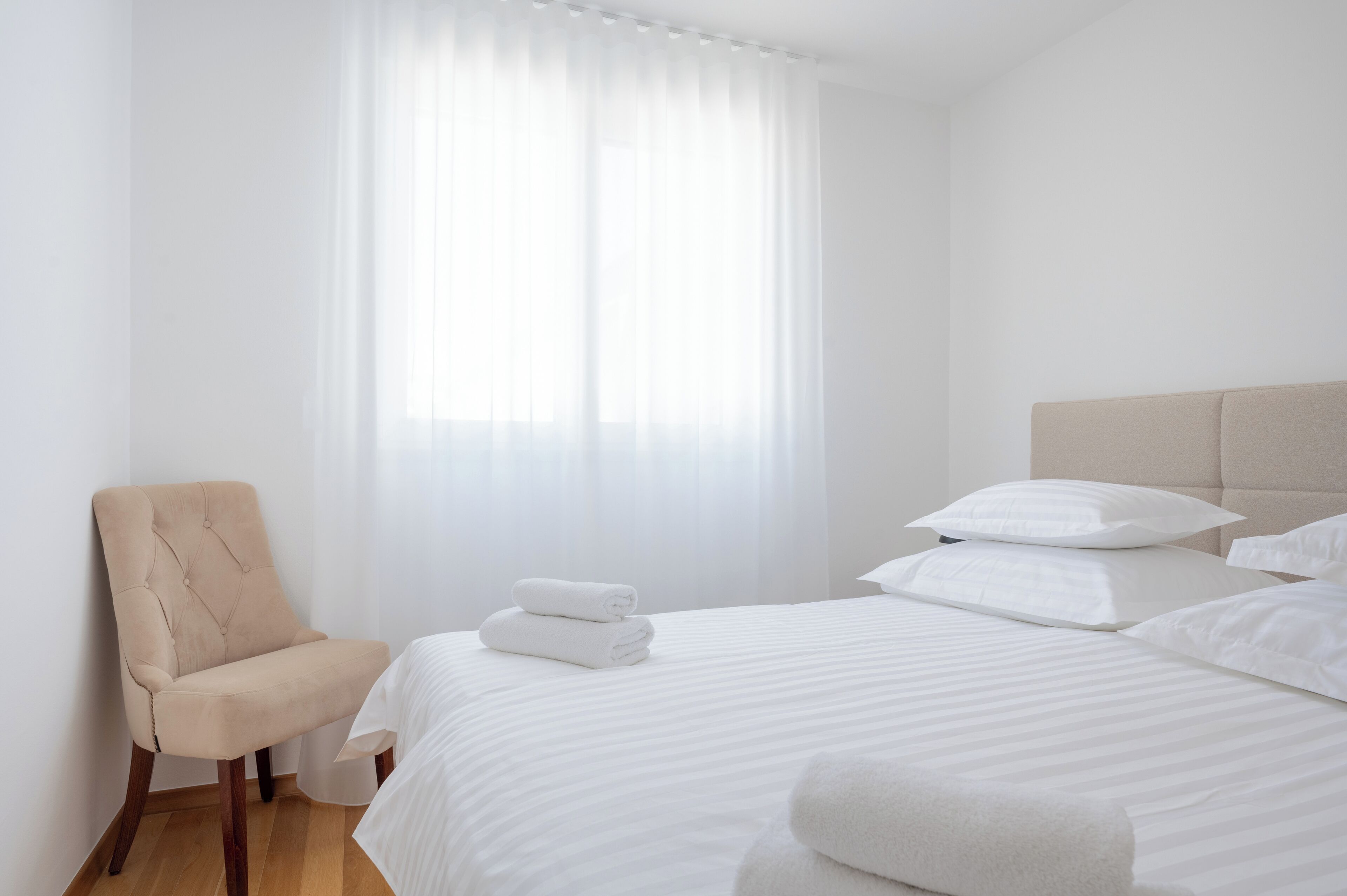 Een hotelkamer met een bed, een stoel en een raam met dunne gordijnen.